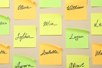 Paper stickers with different names on beige background, flat lay. Choosing baby's name