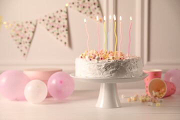 Tasty Birthday cake with burning candles and party decor on white table