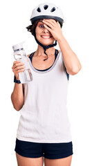 Beautiful young woman with short hair wearing bike helmet and holding water bottle stressed and frustrated with hand on head, surprised and angry face