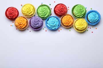 Many tasty cupcakes with bright cream and sprinkles on white background, flat lay. Space for text