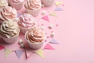 Delicious birthday cupcakes, bunting flags, marshmallows and sprinkles on pink background. Space...