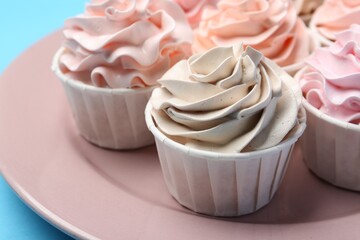 Plate with tasty cupcakes on light blue background, closeup