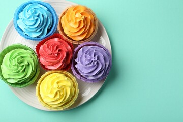 Plate with delicious bright cupcakes on turquoise background, top view. Space for text