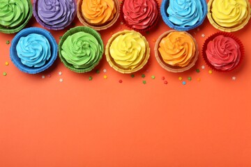 Delicious bright cupcakes and sprinkles on coral background, flat lay. Space for text