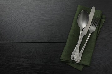Stylish setting with cutlery and napkin on black wooden table, top view. Space for text