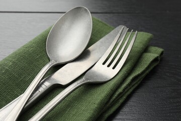 Stylish setting with cutlery and napkin on black wooden table, closeup