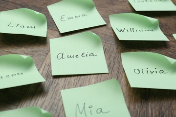 Paper stickers with different names on wooden table, closeup. Choosing baby's name