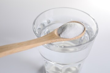 Spoon with baking soda over glass of water on white background, closeup