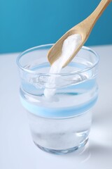 Adding baking soda into glass of water on color background, closeup