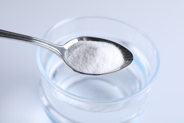 Spoon with baking soda over glass of water on light background, closeup