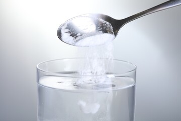 Adding baking soda into glass of water on light grey background, closeup