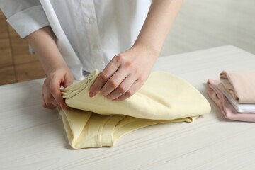 Woman folding clothes at white wooden table indoors, closeup