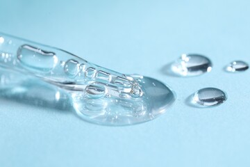 Glass pipette and transparent liquid on light blue background, closeup