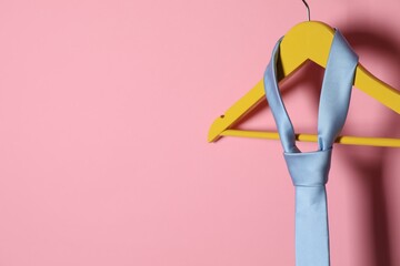 Hanger with light blue tie on pink background. Space for text