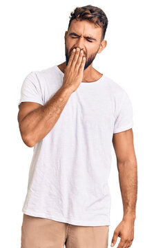 Young hispanic man wearing casual white tshirt bored yawning tired covering mouth with hand. restless and sleepiness.