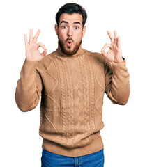 Naklejka premium Young hispanic man wearing casual clothes looking surprised and shocked doing ok approval symbol with fingers. crazy expression