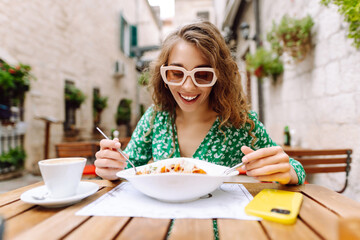 Young woman sitting in summer cafe, eating pasta with tomato, meat. Bolognese. Parmesan cheese....
