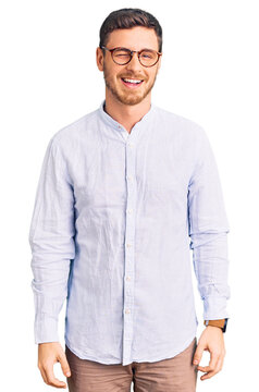 Handsome young man with bear wearing elegant business shirt and glasses winking looking at the camera with sexy expression, cheerful and happy face.