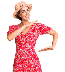 Naklejka premium Young beautiful woman wearing summer hat gesturing with hands showing big and large size sign, measure symbol. smiling looking at the camera. measuring concept.
