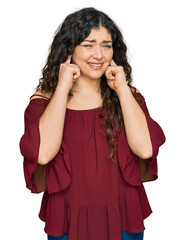 Young hispanic girl wearing casual clothes covering ears with fingers with annoyed expression for the noise of loud music. deaf concept.