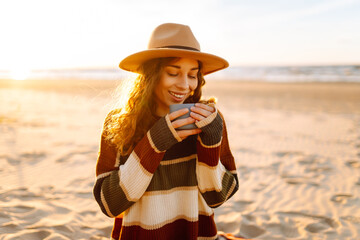 Young woman sits at picnic on the beach drinks a hot drink from a thermos. A girl enjoying...