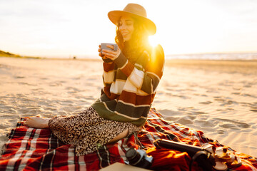 Young woman sits at picnic on the beach drinks a hot drink from a thermos. A girl enjoying...