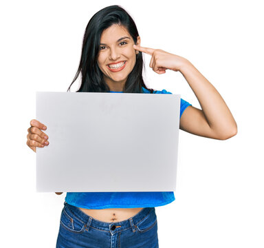 Young hispanic woman holding blank empty banner pointing finger to one self smiling happy and proud