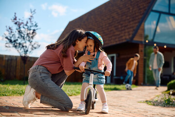 Happy mother teaching her small daughter to ride bicycle in  backyard.