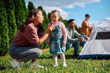 Fototapeta premium Little girl and her mother blowing dandelion during family day in nature.