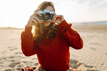 Fototapeta premium Young woman traveler is taking pictures of nature on retro camera in picnic at the beach. Trip, photography or girl with nature.