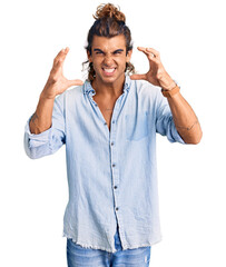 Young hispanic man wearing summer style shouting frustrated with rage, hands trying to strangle, yelling mad