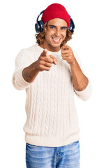 Young hispanic man listening to music using headphones pointing fingers to camera with happy and funny face. good energy and vibes.