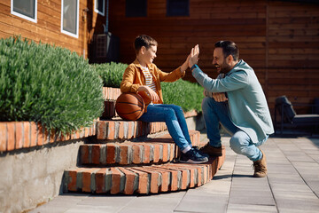 Happy father and son giving high-five after playing basketball in backyard. Copy space.