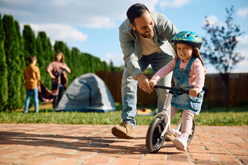 Happy little girl having fun while her father is teaching her to ride bicycle in nature.