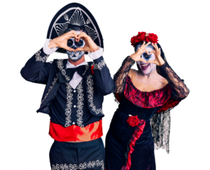 Young couple wearing mexican day of the dead costume over background doing heart shape with hand and fingers smiling looking through sign