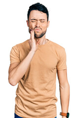 Hispanic man with beard wearing casual t shirt touching mouth with hand with painful expression because of toothache or dental illness on teeth. dentist