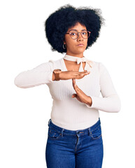 Young african american girl wearing casual clothes and glasses doing time out gesture with hands,...