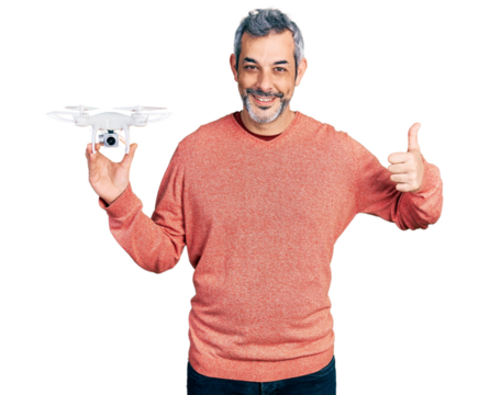 Middle age hispanic man with grey hair holding drone smiling happy and positive, thumb up doing excellent and approval sign
