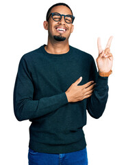Young african american man wearing casual clothes and glasses smiling with happy face winking at...