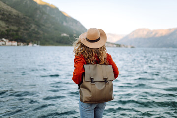 Young woman with backpack near lake on wooded mountains background. Amazing landscape. Enjoying nature. Concept of weekends trip.