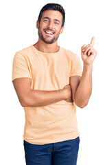 Fototapeta premium Young hispanic man wearing casual clothes with a big smile on face, pointing with hand and finger to the side looking at the camera.