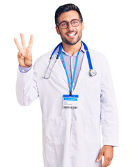 Young hispanic man wearing doctor uniform and stethoscope showing and pointing up with fingers number three while smiling confident and happy.