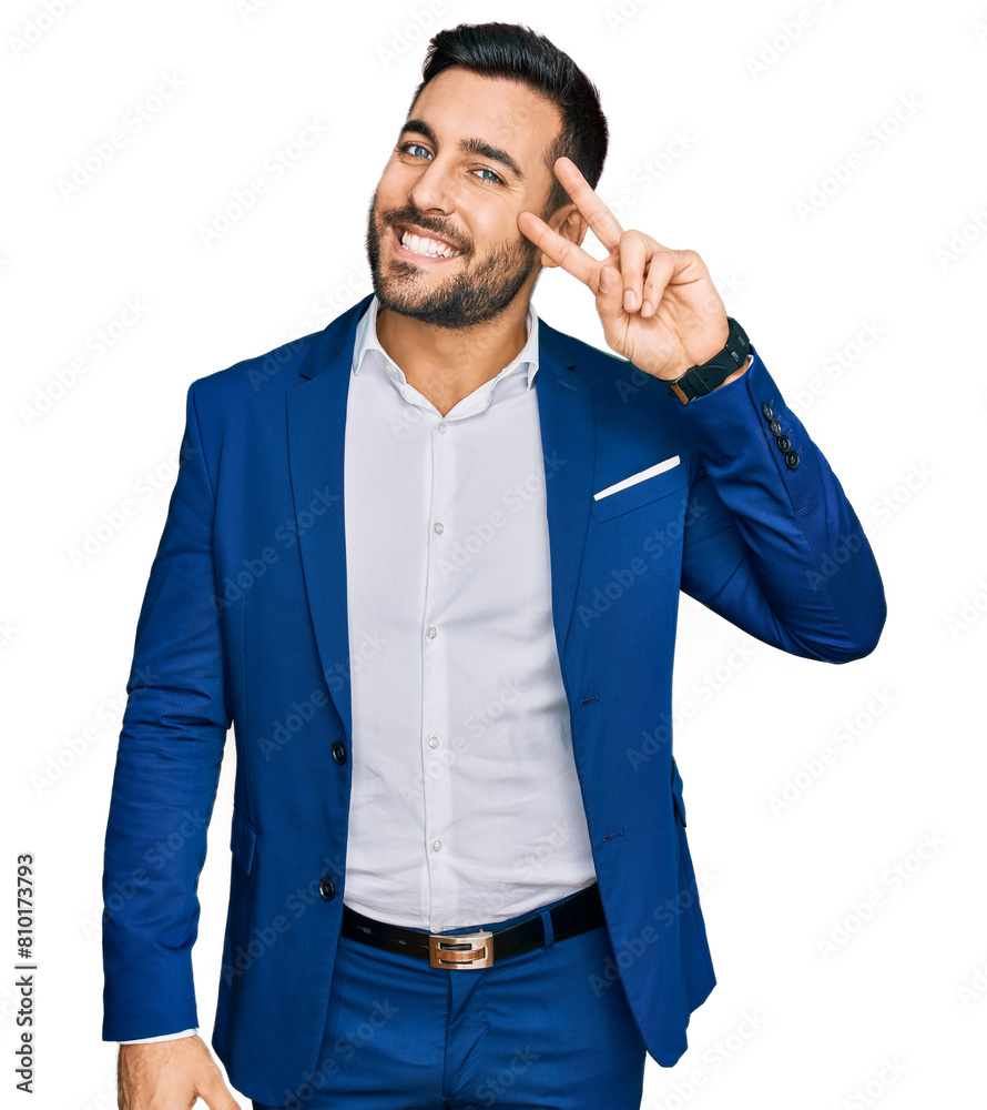 Sticker Young hispanic man wearing business jacket doing peace symbol with fingers over face, smiling cheerful showing victory