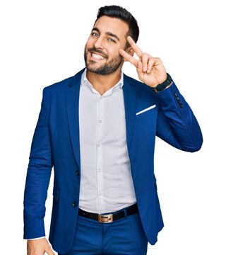 Young hispanic man wearing business jacket doing peace symbol with fingers over face, smiling cheerful showing victory