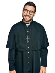 Young hispanic man wearing priest uniform looking positive and happy standing and smiling with a...