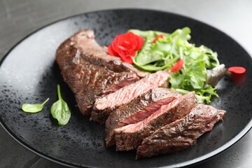 Pieces of delicious grilled beef meat and greens on table, closeup