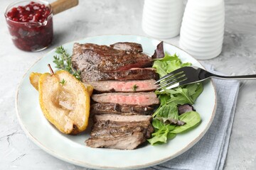 Delicious roasted beef meat, caramelized pear and greens served on light table, closeup