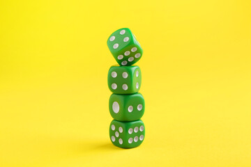 Many stacked green game dices on yellow background, closeup