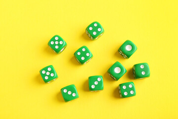 Many green game dices on yellow background, flat lay