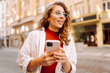 Beautiful smiling woman using phone walking in city street. Business, education, technology,...